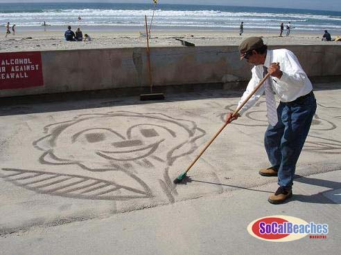 Albert "The Mission Beach Sandman" uses his broom to create another sand cartoon on the sidewalk and boardwalk. Photo Copyright Sean Callahan & Mission Beach Online.com